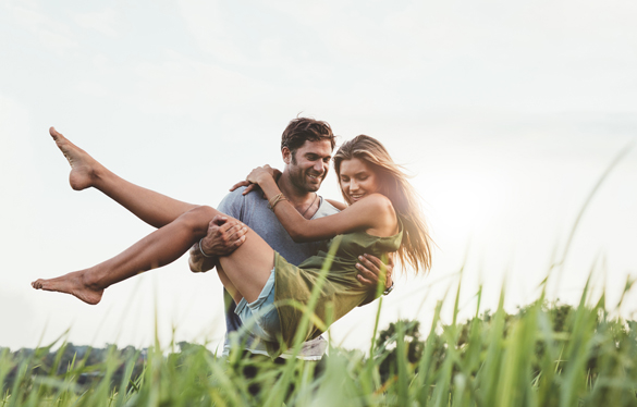 Shot of young man carrying his beautiful girlfriend in arms and walking through grass field - Reasons To Date A Scorpio Man