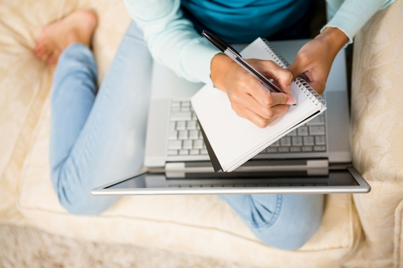 Mid section of woman writing on notepad with laptop on her legs while sitting on the sofa - Is It Possible To Get a Scorpio Man To Change His Mind